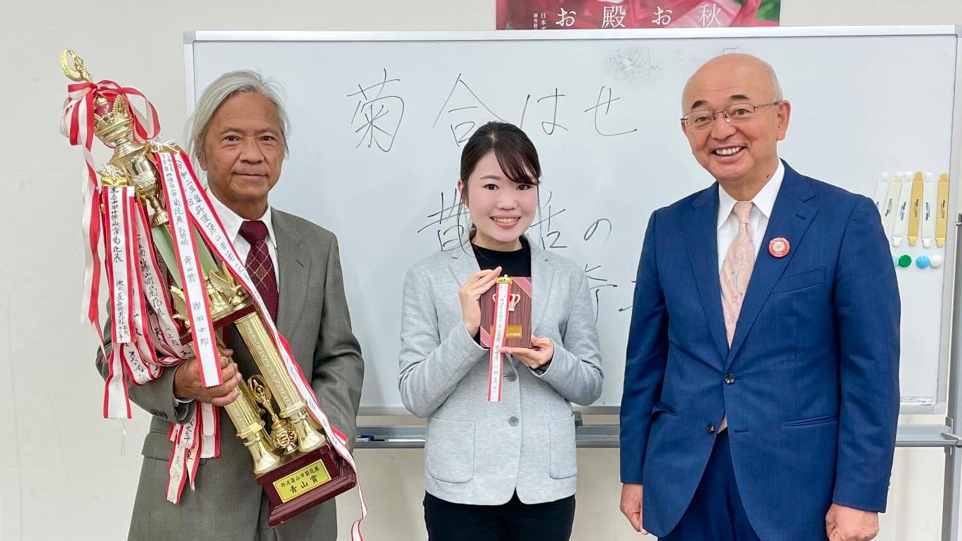 左端にトロフィーを持った男性、真ん中に盾を持った女性、右端に市長が立っている