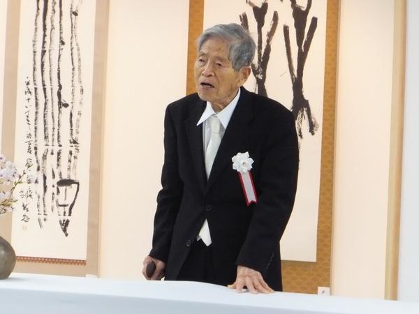 三宅 剣龍先生が、左手を机の上に添え、立って発言している写真