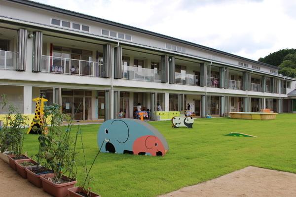 芝生にぞうさんやキリンの遊具があり、奥には横長の建物が建っている写真