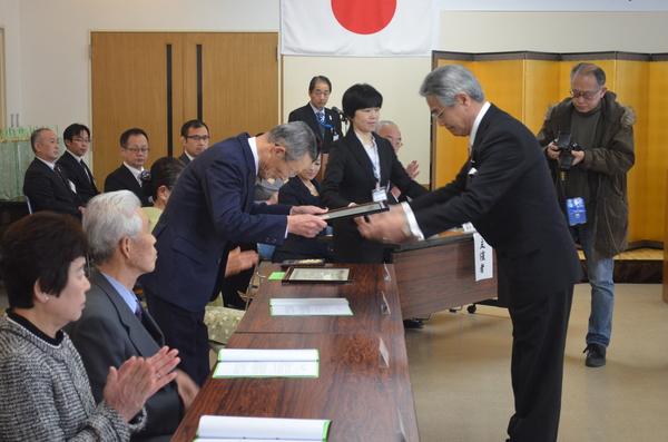 年配の男性が頭を下げながら賞状を受け取っているのを横からうつした写真