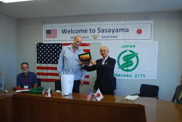 市長が夜景画の額を手に持ち委員長のフランクリン・ディーンさんと一緒に記念撮影写真