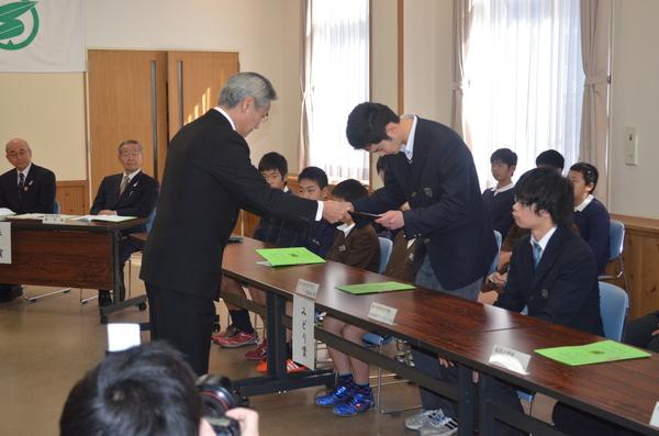制服姿の男子学生2人のうち1人が立ち上がり賞状を受け取っている写真