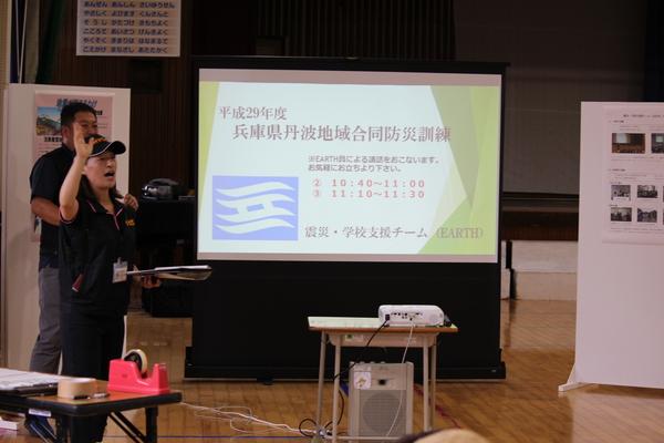 兵庫県丹波地域合同防災訓練と書かれたモニターの手前で帽子をかぶった女性が説明をしている写真