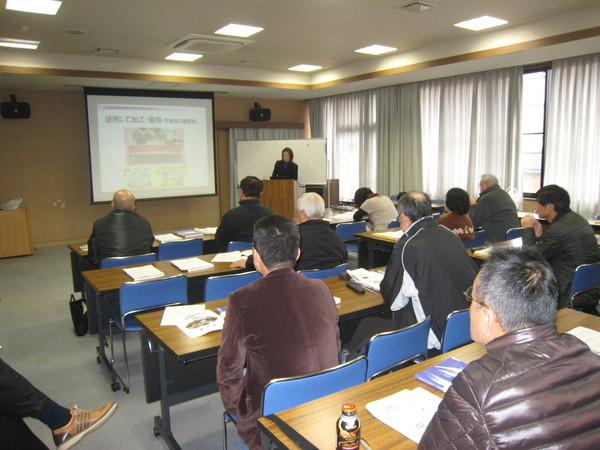 黒いジャケットを着た女性が壇上に立ち最後の講義で農産物の付加価値化（6次産業化）についての説明を熱心に聞いている受講生の後ろ姿の写真