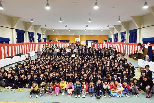 体育館で、ポーズをとる生徒と教師、地域の皆さんの集合写真