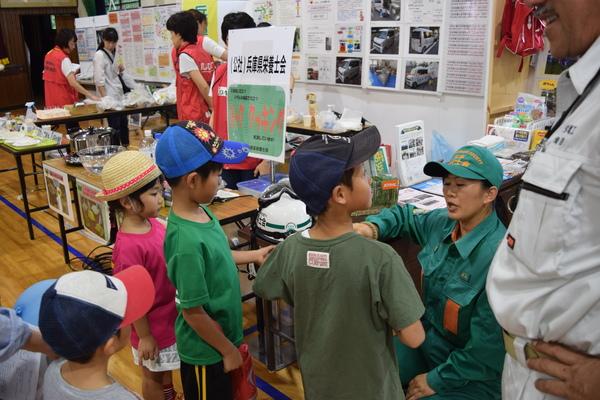 兵庫県栄養士会と書かれた立て札が立っている机の周りに子供たち4名が立っていて、作業着を着た女性が子供たちに説明をしている写真