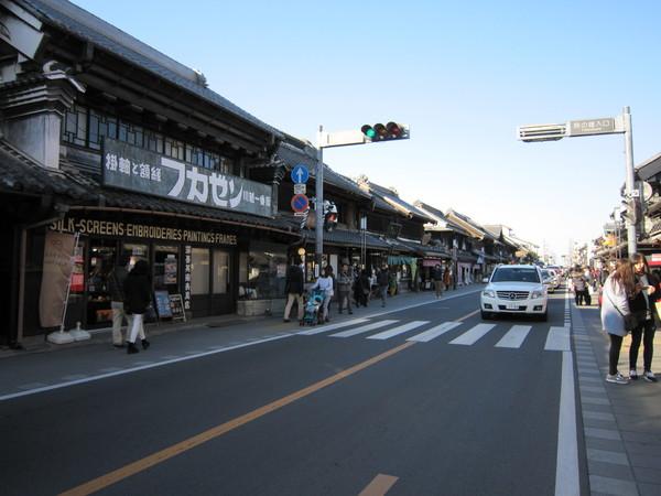 古い商店街が建ち並び歩道にはたくさんの人が歩いて車が走っている写真