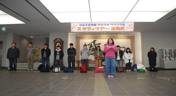 短期交換留学生が後ろに並び、ピンクにジーンズの洋服を着た女性がマイクを持ち話をしている写真