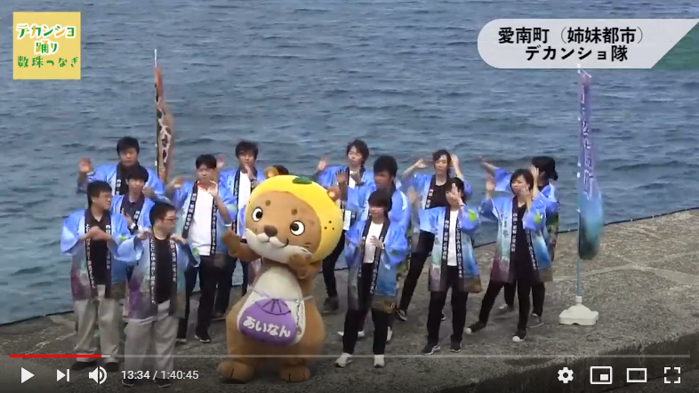 法被を着た愛南町デカンショ隊十数名とマスコットキャラクターなーし君が浜辺でデカンショを踊っている
