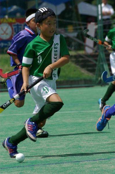 9の数字が入ったユニフォームを着た少年がスティックを持って走っている写真