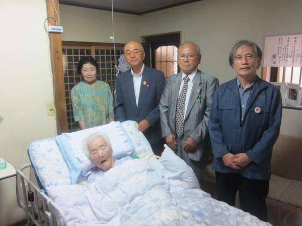 介護ベッドで起き上がっている長寿祝いの辻しげ子さん(103歳)が市長らと一緒に写っている写真
