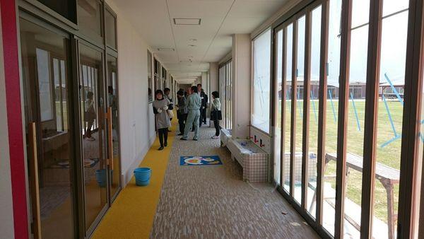 まだらな模様のはじに黄色の線が引かれている廊下の上を6名ほどの人達が歩いて見学している写真
