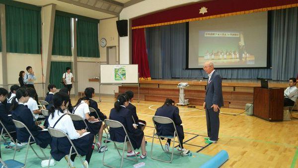 市長がスクリーンを使い、体育館で授業を聞いている城北畑小学校の生徒の写真