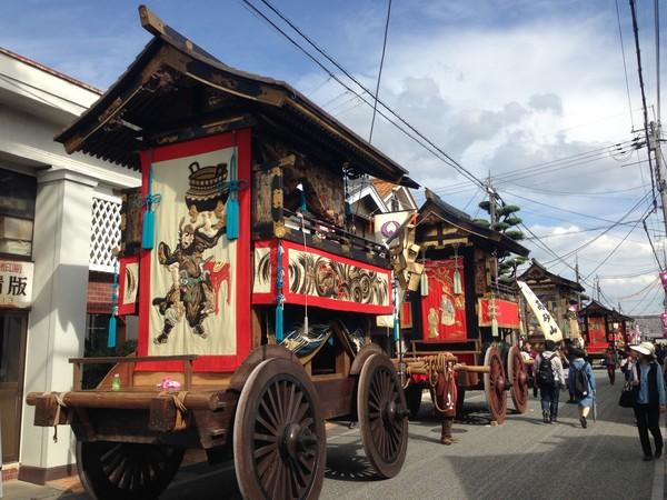 赤い大きな山車が何台も通っている写真