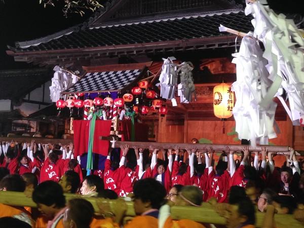 赤い法被を着た男性が大きな神輿をみんなで担いでいる写真