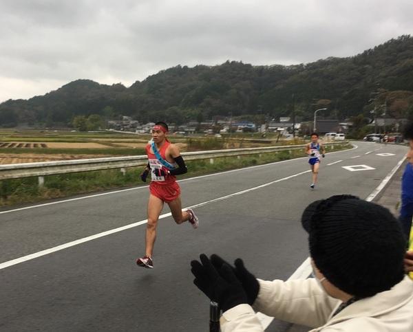 赤いユニフォームを着た井谷 聡志君が、女性が拍手で応援する中走り抜けている写真