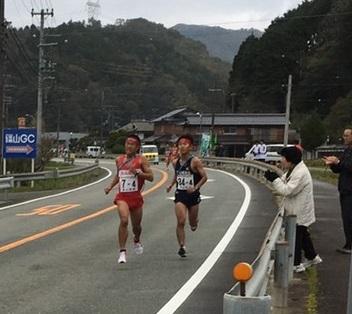 応援している女性の横を、赤いユニフォームを着た篠山鳳鳴高の選手と、黒いユニフォームの選手と互角に走っている写真