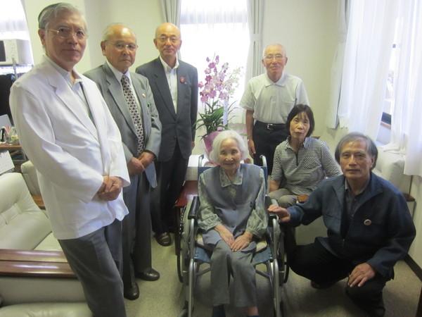 車いすに座っている中山千代子さん(102歳)が長寿祝いの花をバックに市長らと一緒に写っている写真