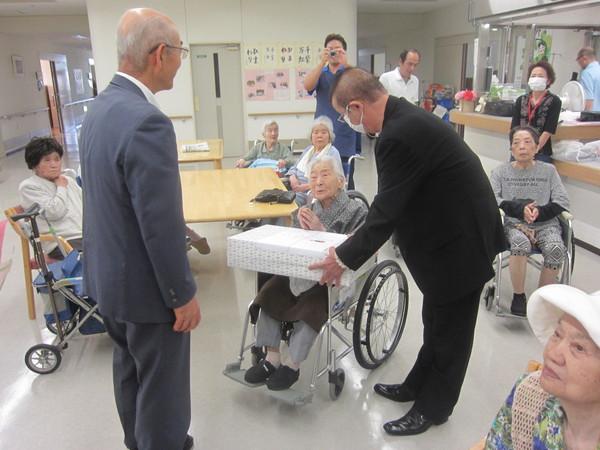 車いすに座っている中西悦子さん(102歳)が長寿祝いの記念品を贈呈されている写真