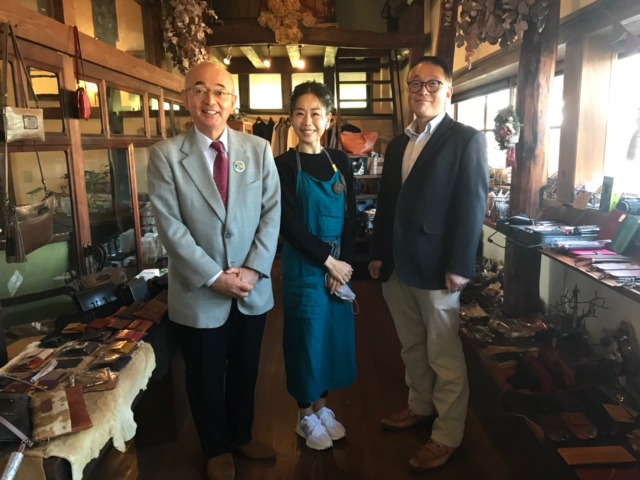 革工房内で、エプロンを着けた女性の職人と市長たちの記念撮影