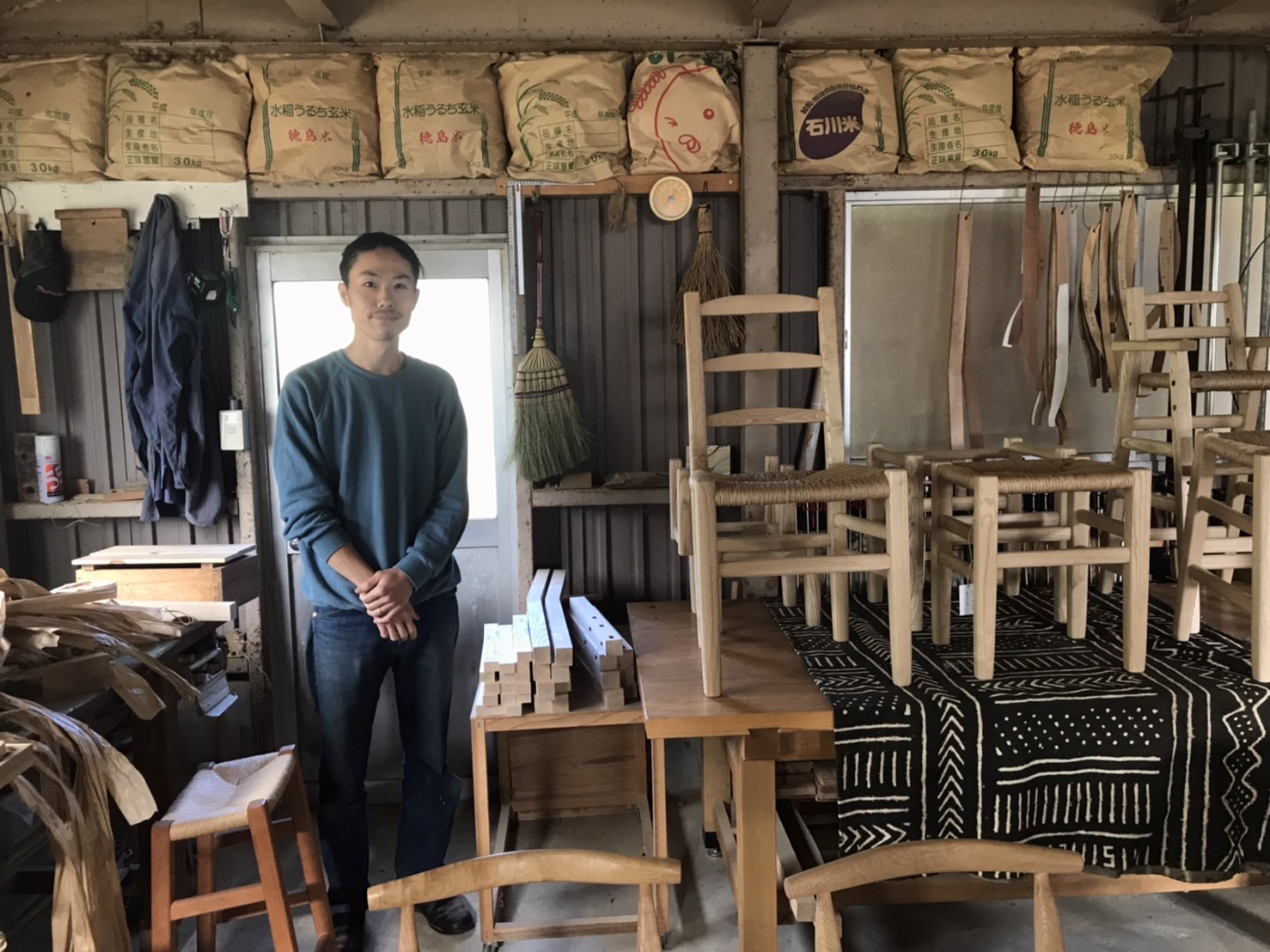 作業机の上にたくさんの椅子が並んでいて、そばに職人の男性が立っている