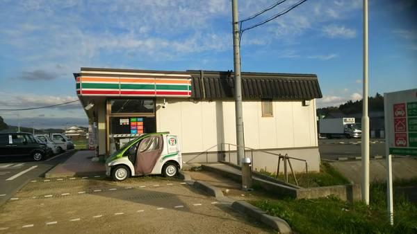 瓦屋根風のセブンイレブンの前に、セブンイレブンの小さい車が止まっている写真