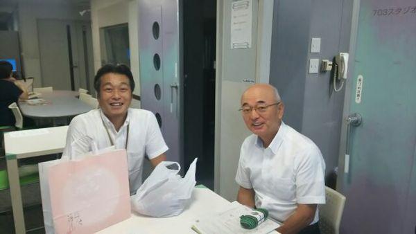 白いテーブルに市長とラジオ局長が二人笑顔で座っている写真