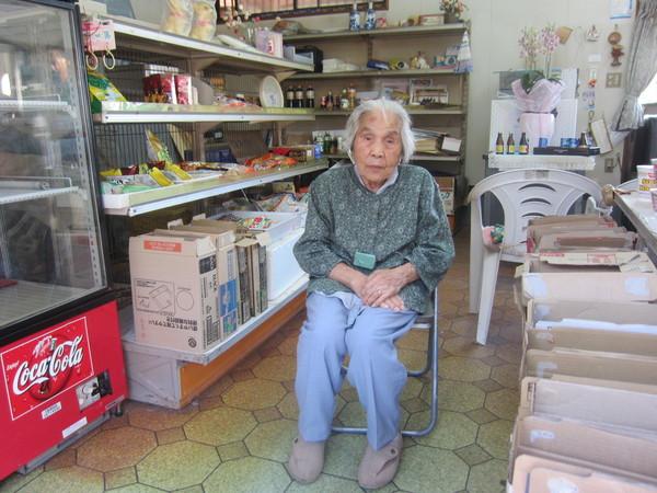パイプ椅子に腰かけている長寿祝いの上田ふみこさん(101歳)が店内で記念撮影している写真