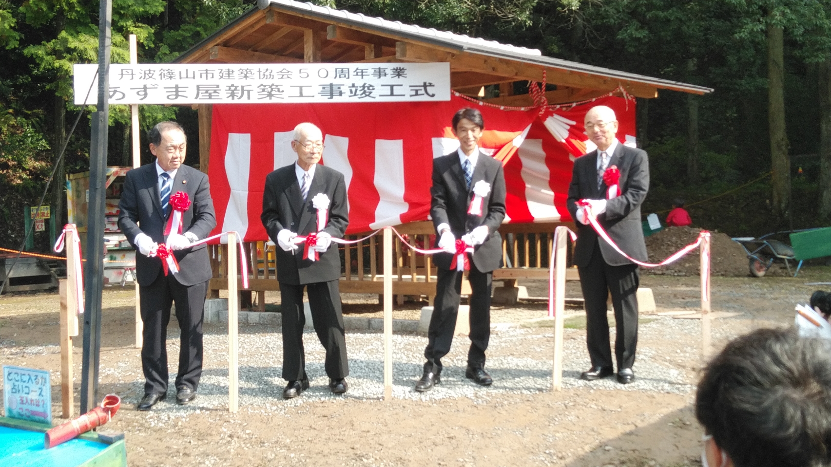 完成したあずま屋の前で、関係者4名がテープカットをしようとしている