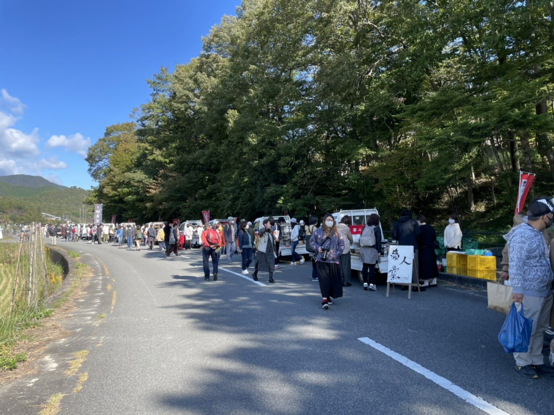 道路に軽トラが並んでおり、荷台には陶器が置いてある。お客様がどれにしようかと迷っている。