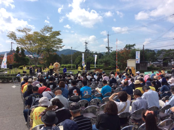 青空の下、お客さんは椅子に座りながら音楽祭を楽しんでいる写真
