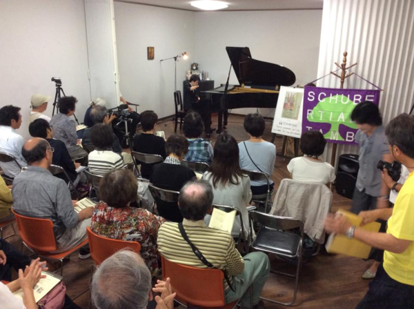 お客さんが椅子に座りピアノの演奏を聞いている写真