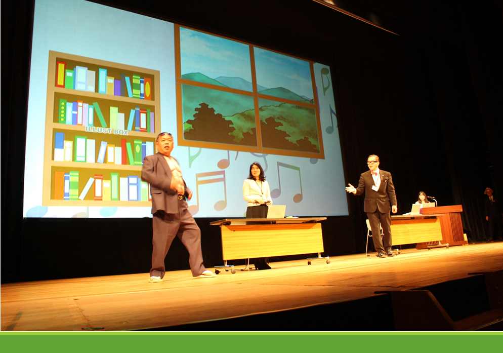 黒色のスーツに赤い蝶ネクタイ姿の秘書課長が、ムキムキ風のTシャツの上にスーツをきた市民役の人に向かって話している写真