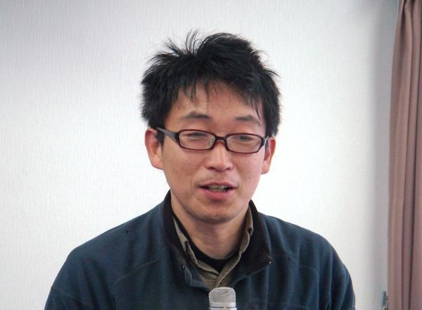 メガネを掛けており、マイクを持って話をしている竹内 照尚さんの写真