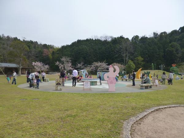 お年寄りがベンチに腰掛け広場では親子が楽しんでいる写真