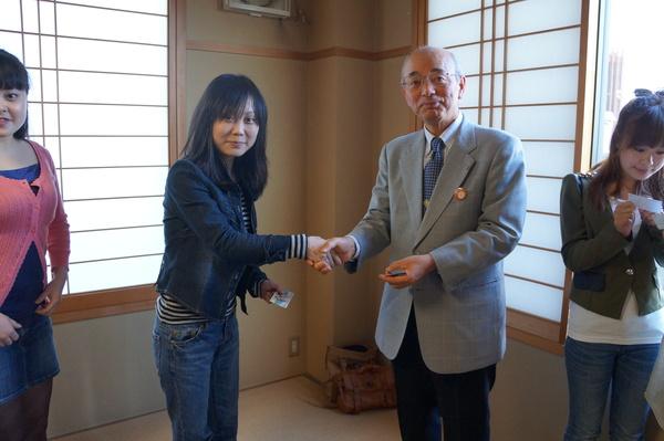 黒のジャケットにジーンズの女性と市長が握手している写真