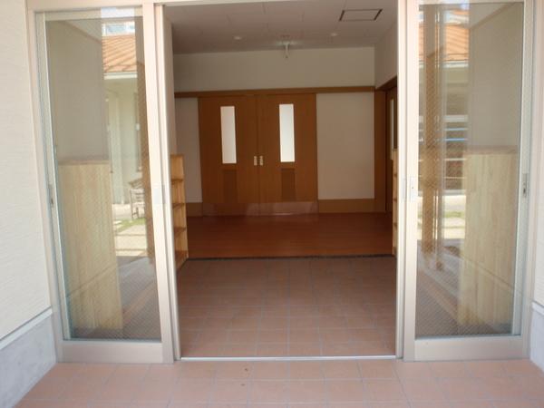 レンガ調の床の横に靴箱があり、奥にドアのあるリハビリ棟の入り口の写真