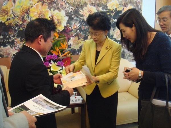 黄色のジャケットにブローチを付けた女性が、大連市副議長に丹波焼を贈呈している写真