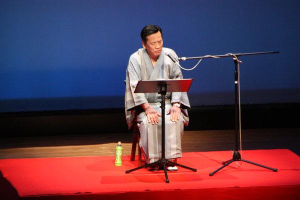 南条 好輝さんが舞台の上で椅子に座り語り芝居をしている写真