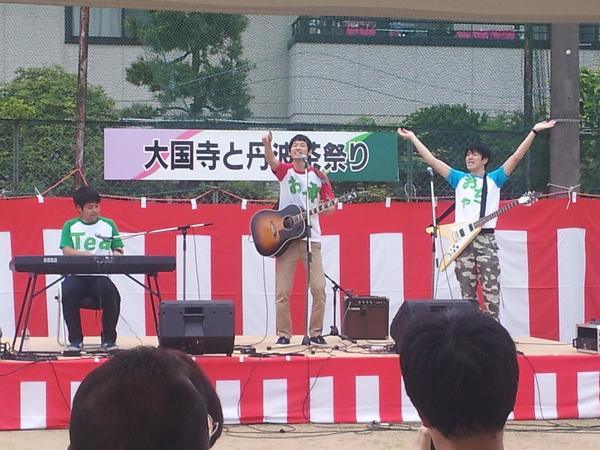 ステージ上でギターやエレクトーンなどの楽器を演奏し、見に来た観客に話しかけている写真