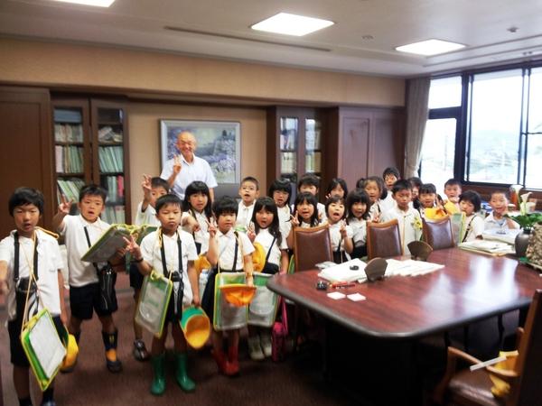 市役所の庁舎見学に来た小学生たちが、一室で市長と一緒にピースサインをしている写真
