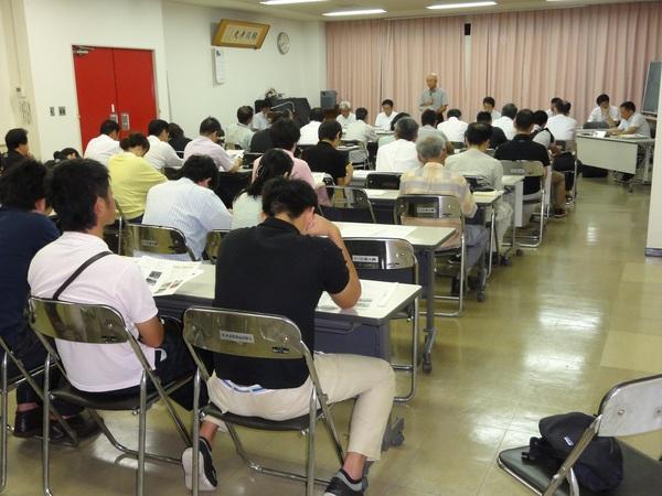 今田会場でたくさんの参加者が長机の資料を見ながら、正面の市長の話を聞いている様子を後ろから写した写真