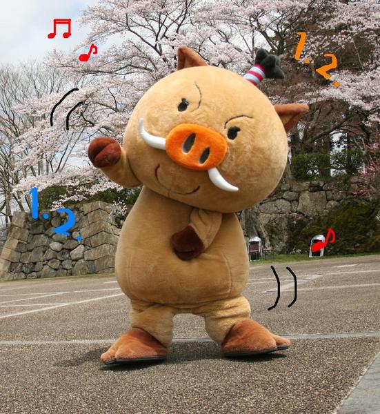 桜の木の前でまるいのの着ぐるみが体を傾けていて、1.2の数字や音符が書かれている写真