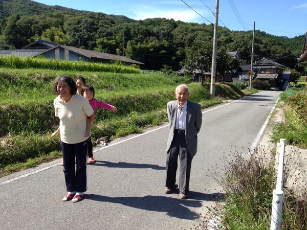 大西 太一郎さんがひ孫の美幸（みこ）ちゃんと一緒に道路でお見送りしている様子の写真