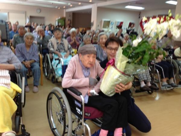 久米 君子さんが花の鉢植えをもらっている写真