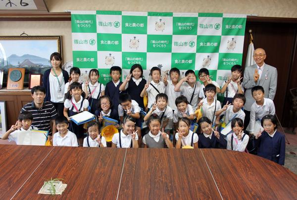 13名の男子児童と13名の女子児童、男性の先生と女性の先生が左はじにいて、市長と一緒に記念撮影をしている写真