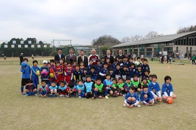 市長とスーツを着た男性とユニフォームや、ビブスをつけて集まる子供たちの集合写真