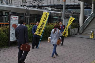 あいさつ運動実施中の黄色い旗を持ち、通りすがりの人に笑顔で挨拶をしている男性2名の写真