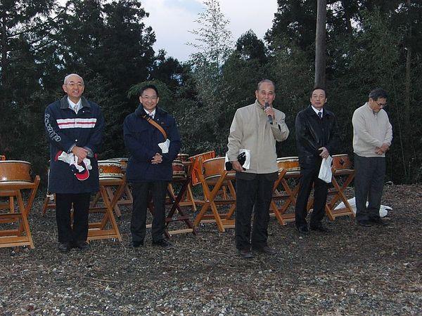 権現山初日を迎える会に市長が参列し代表者の挨拶を左後方で聞いている写真