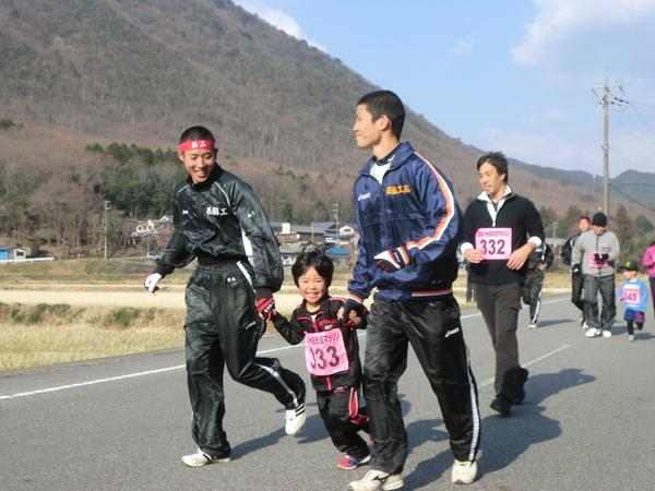 黒のジャージを着た男の子が笑顔で高校生のお兄さんに両手を繋いでもらい一緒に走っている写真